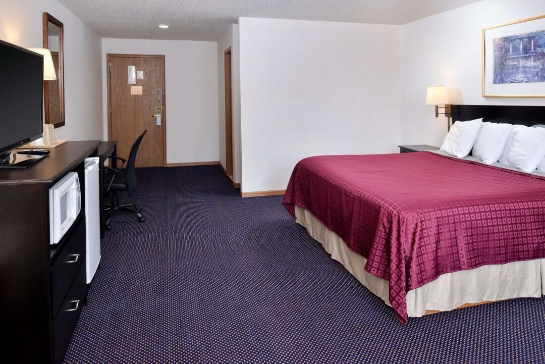 A hotel room with a bed, desk, chair, and a television.