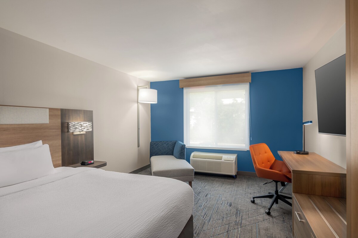 A hotel room with a bed, a desk, a chair, a TV, and a window.