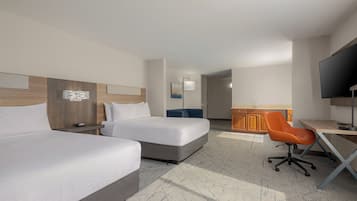 A hotel room with two beds, a desk, a chair, a TV, and a bathroom visible in the background.