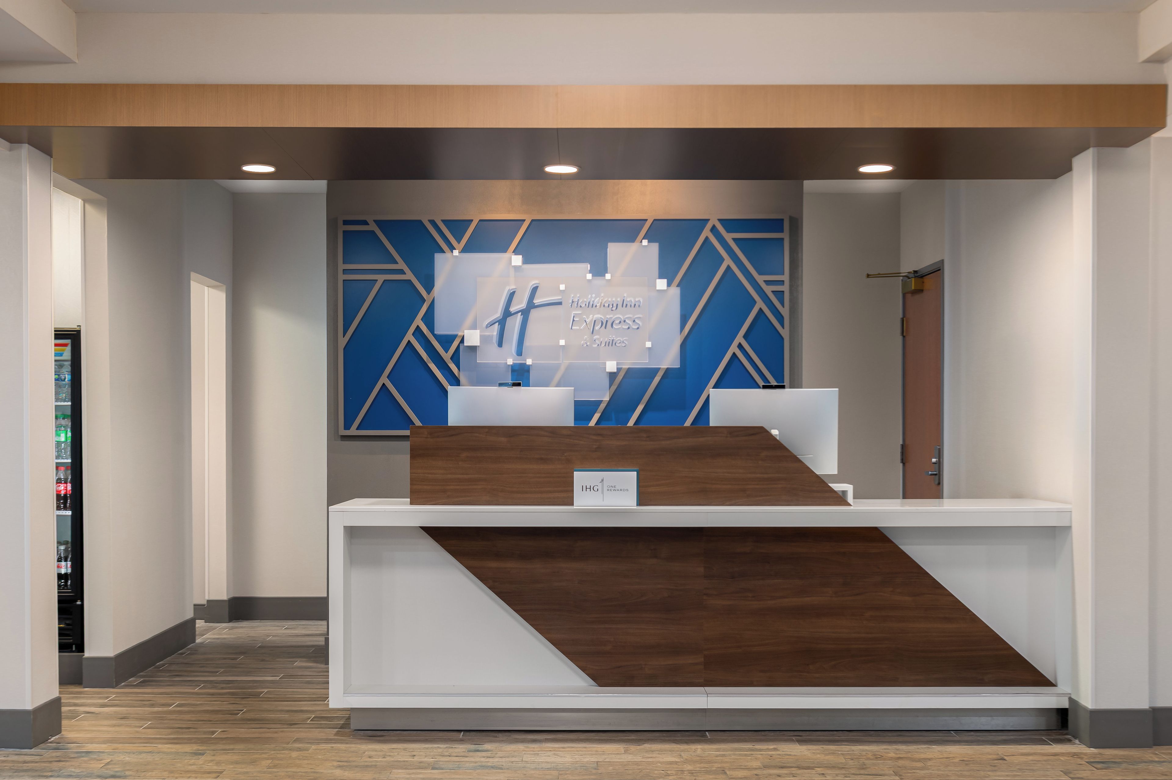 Un mostrador de recepción con un diseño geométrico azul en la pared, un detalle de madera y un letrero de Holiday Inn Express & Suites.
