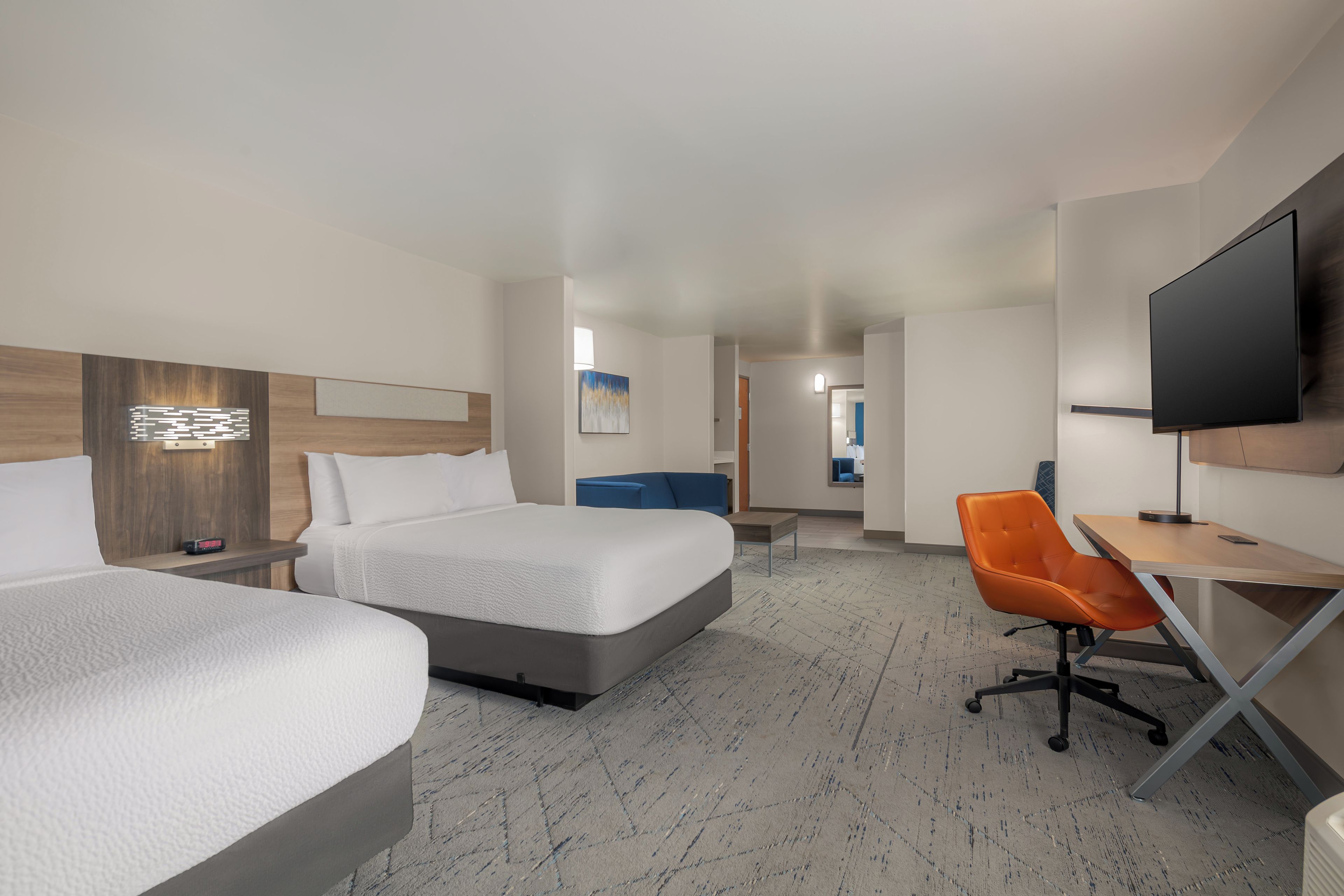 A hotel room with two beds, a desk, a chair, a television, and a painting on the wall.