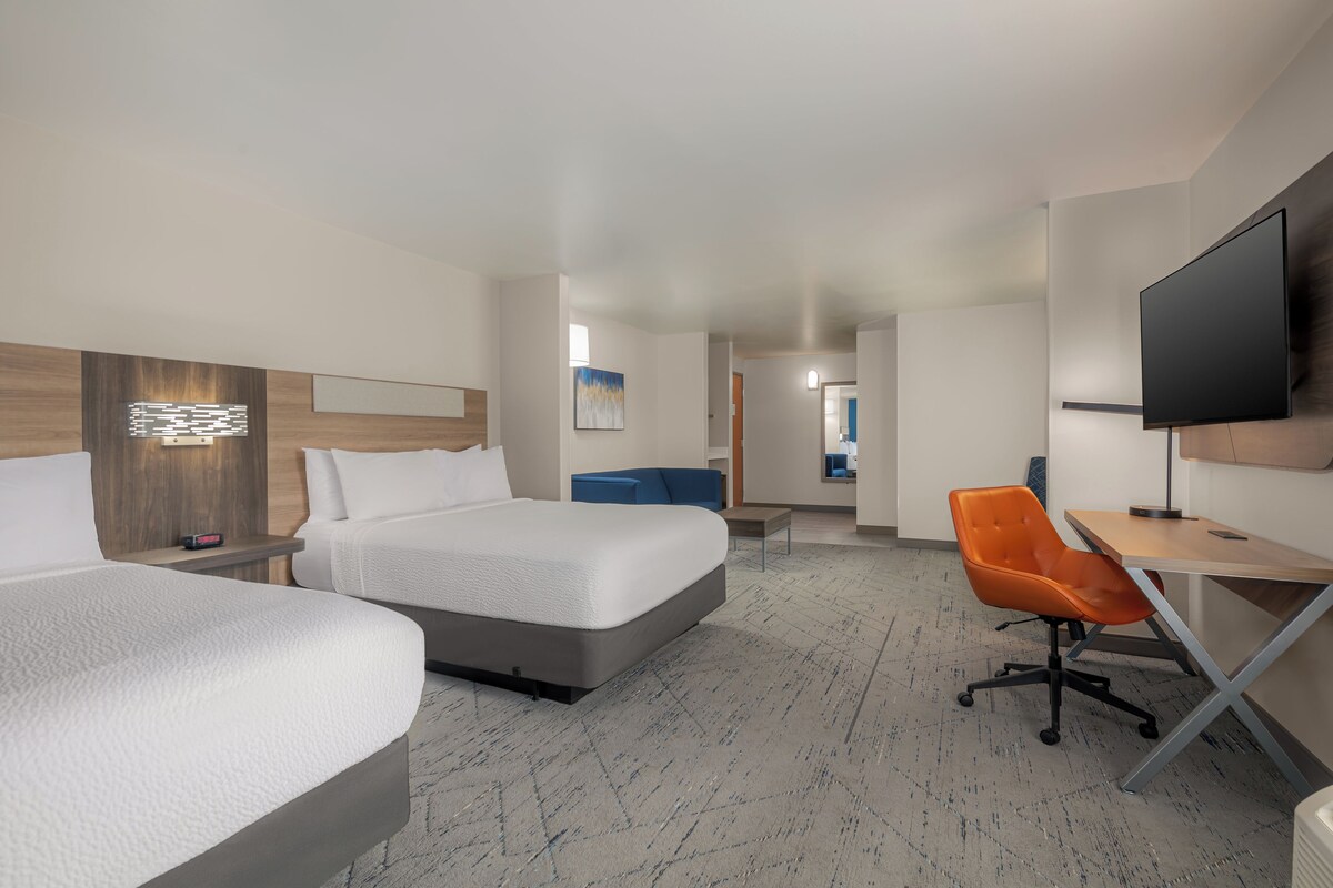 A hotel room with two beds, a desk, a chair, a television, and a painting on the wall.