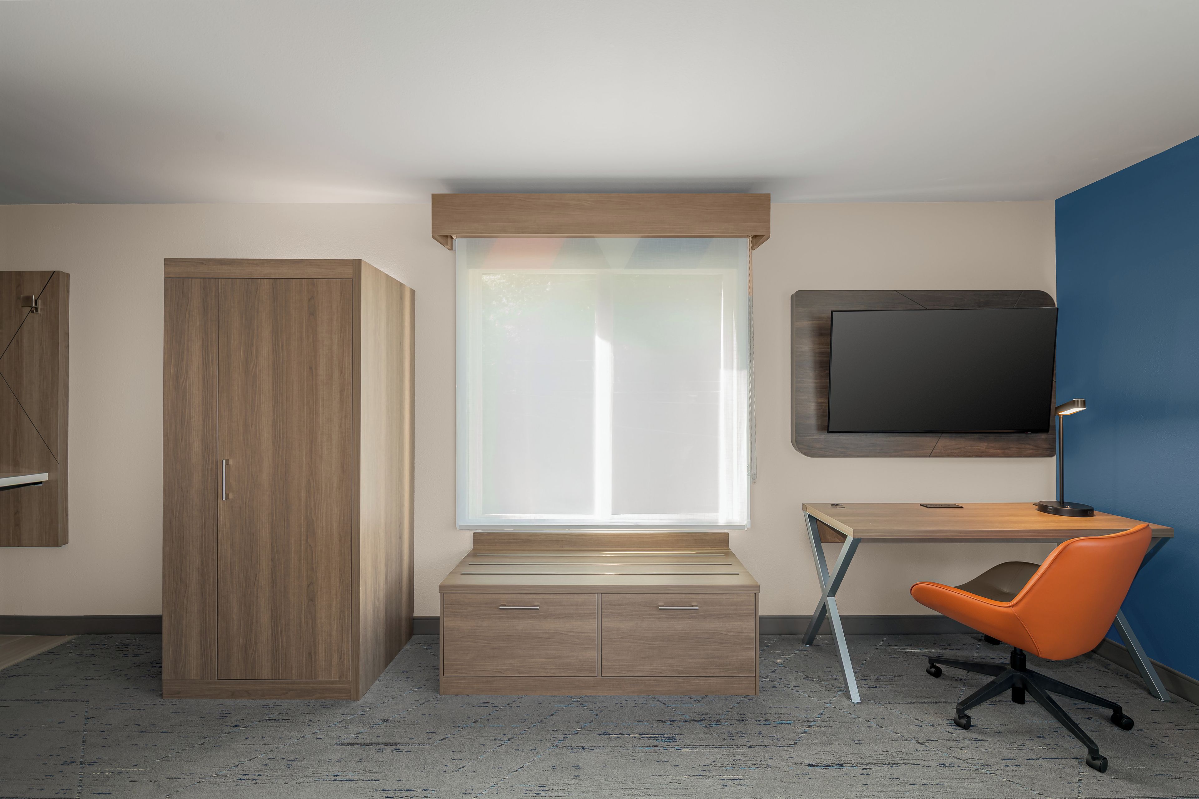 A modern bedroom with a bed, a wardrobe, a desk with a chair, and a television.