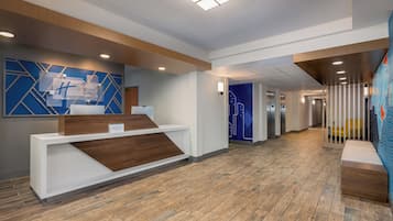 A hotel reception area with a modern design, including a reception desk, a blue wall with geometric patterns, and a wooden floor.