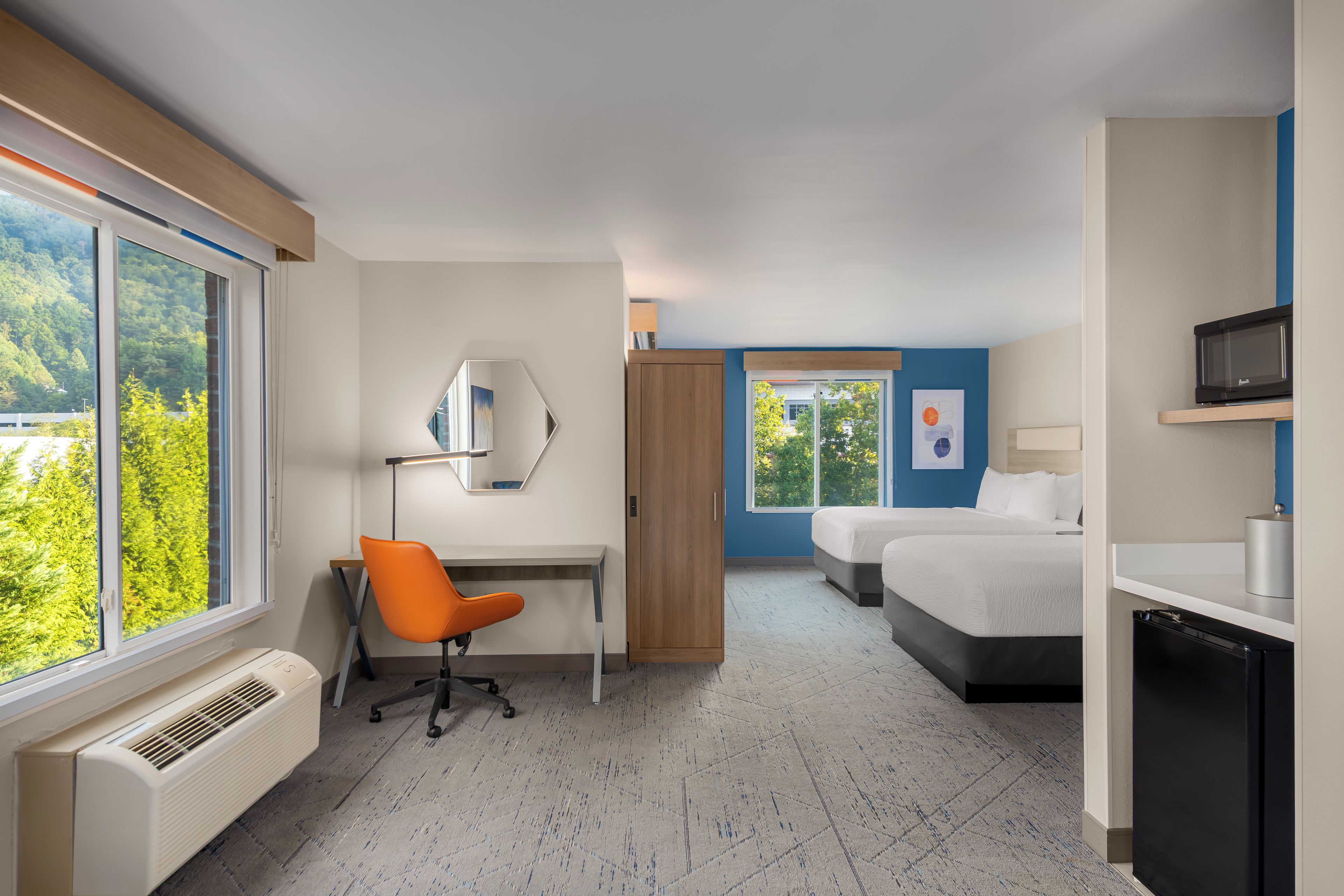 Hotellihuone, jossa on työpöytä, tuoli, kaksi sänkyä, vaatekaappi, televisio ja ikkuna, josta on näkymä puita kohti.