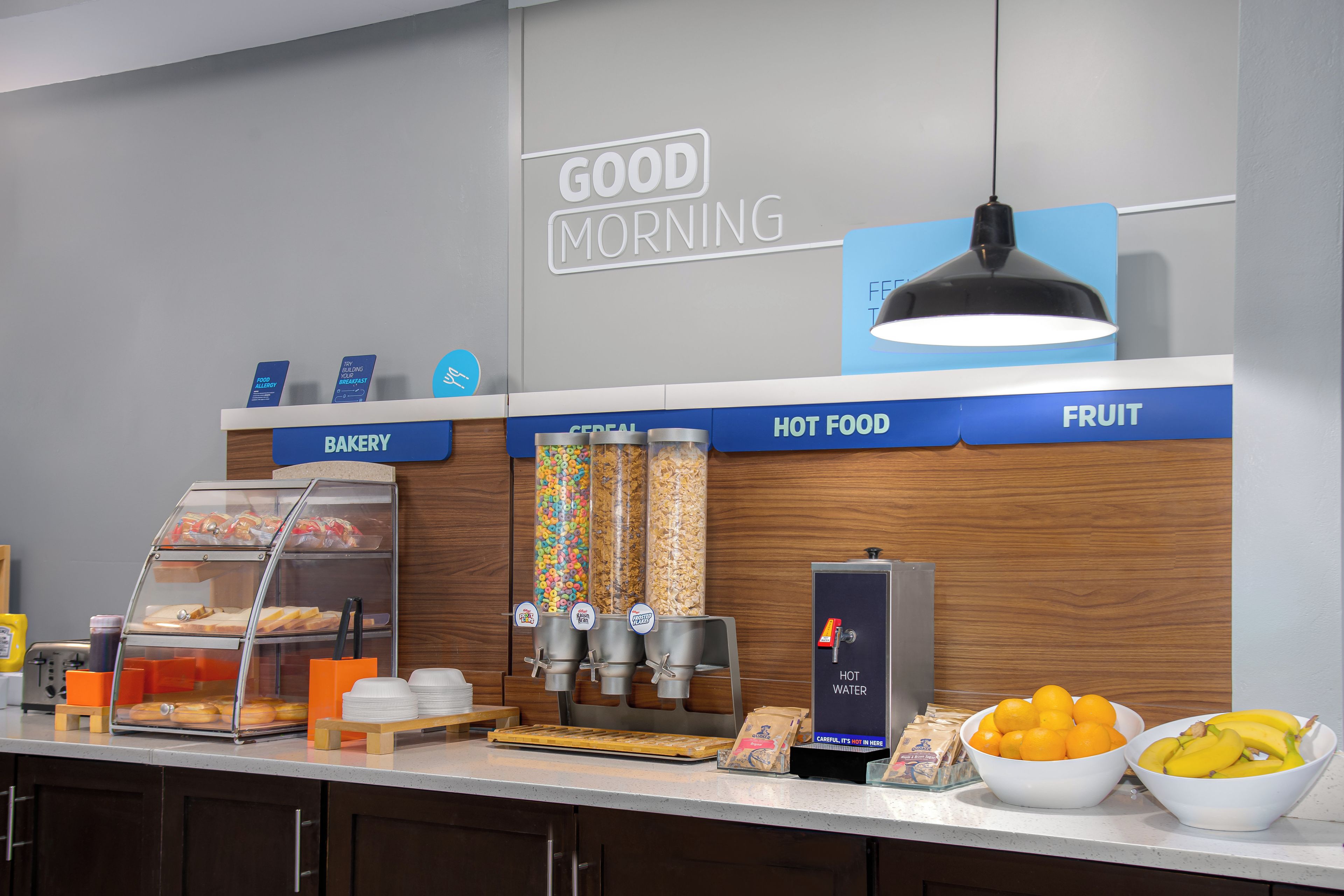 A breakfast bar with labeled sections for bakery, hot food, and fruit.
