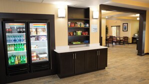 A hotel lobby with a snack bar, a refrigerator stocked with beverages, and a seating area with tables and chairs.