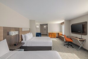 A hotel room with two beds, a desk, a TV, and a bathroom in the background.