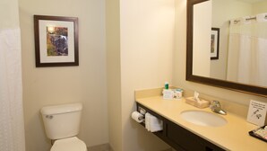 Un baño con inodoro, lavabo, espejo, un cuadro enmarco y un perchero para toallas.