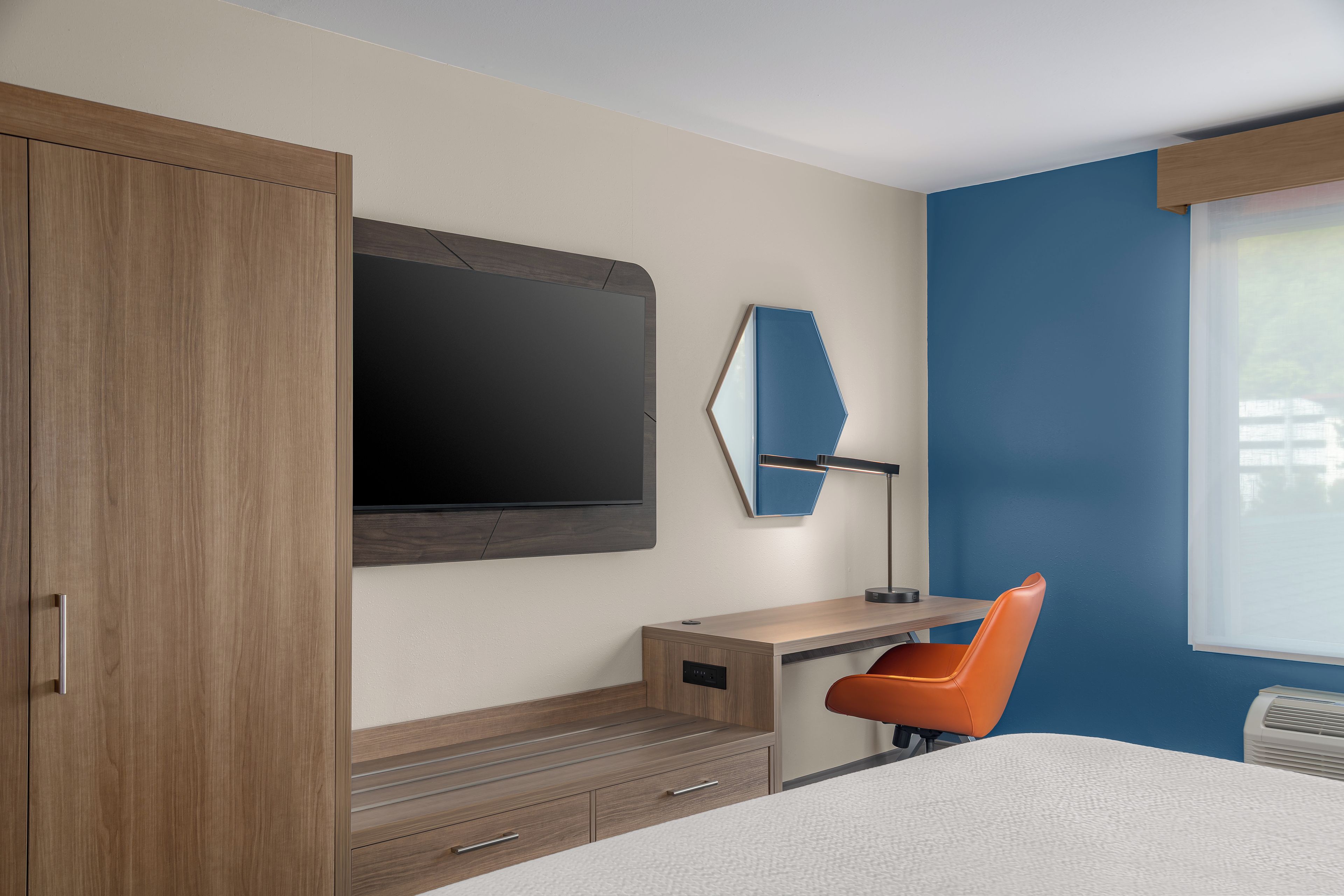 Une chambre à coucher comprenant un lit, un bureau, une chaise, une armoire, un miroir et une fenêtre.