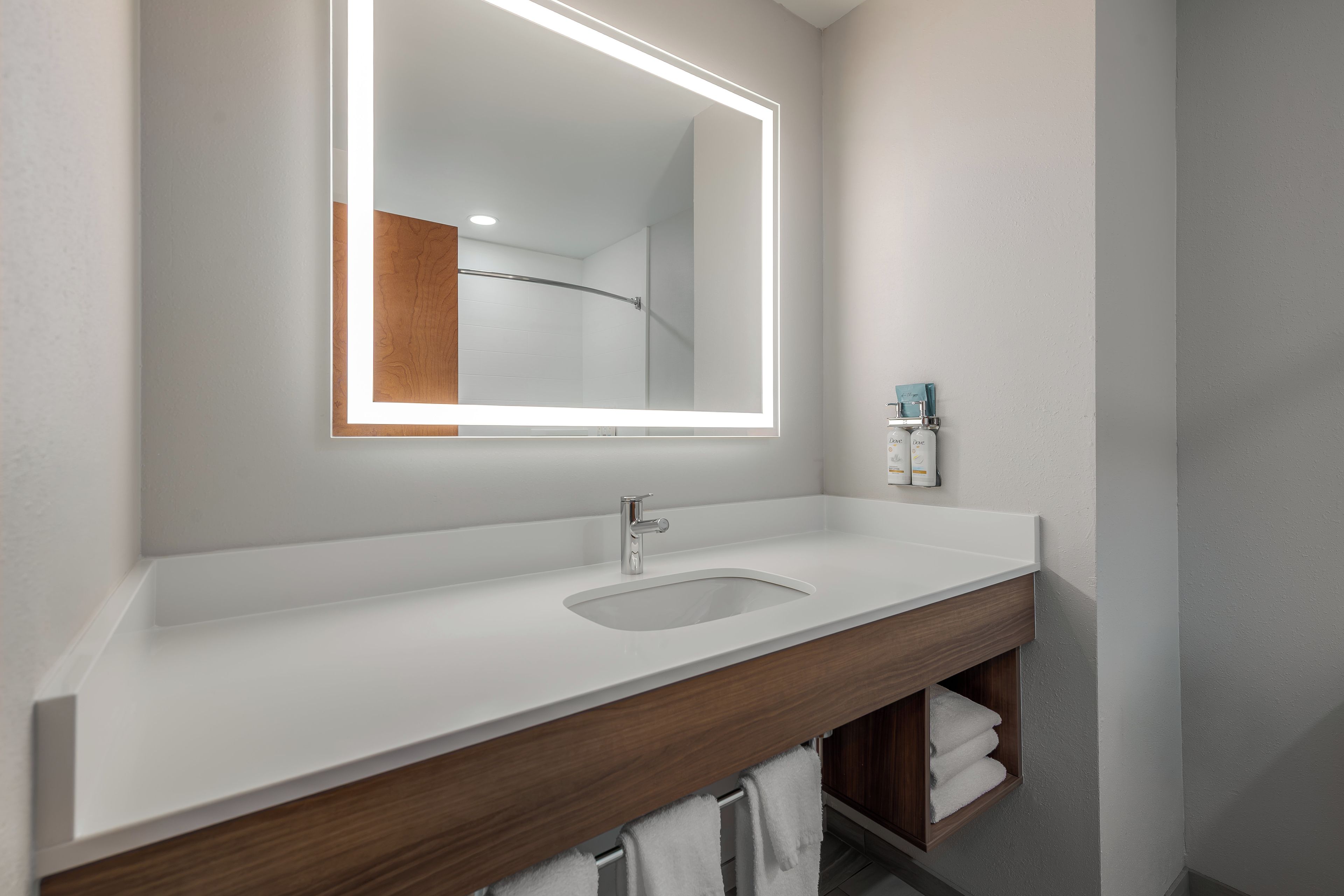 A modern bathroom with a white sink, a large mirror with integrated lighting, and a wooden vanity.