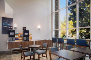 A modern coffee shop interior with seating, coffee machines, and a large window offering a view of trees. - Holiday Inn Express Hotel & Suites Cherokee / Casino by IHG (Cherokee)