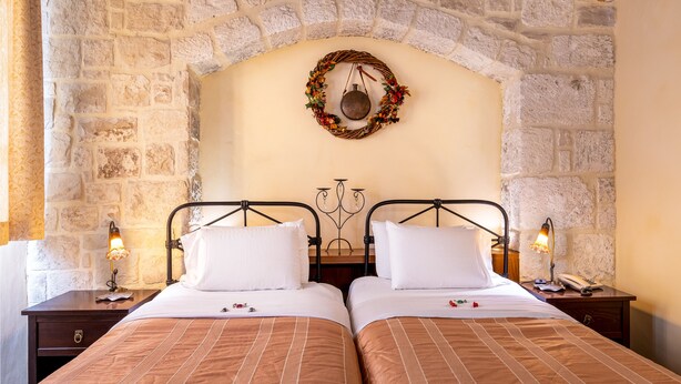 A double bed with a striped bedspread, two bedside tables with lamps, a stone wall, and a decorative wreath on the wall. - Palazzino Di Corina (Rethymno)