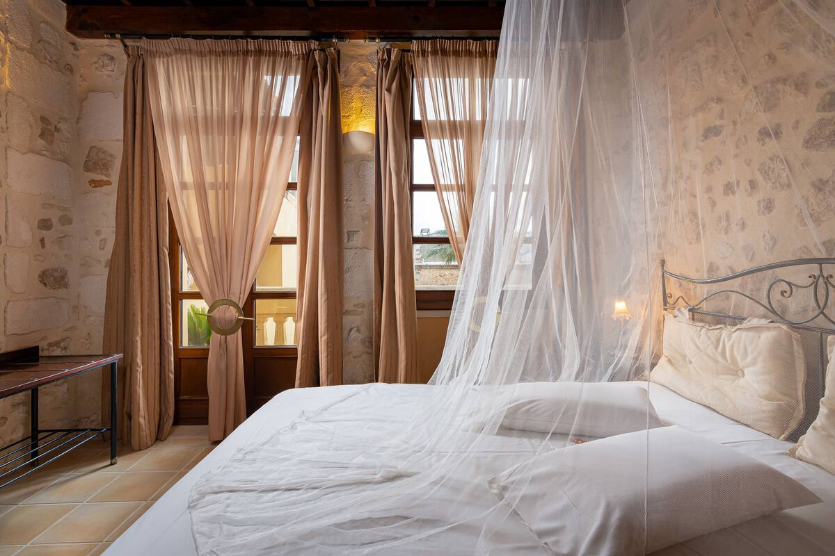 A bedroom with a bed, curtains, a bedside table, and a window with a view.
