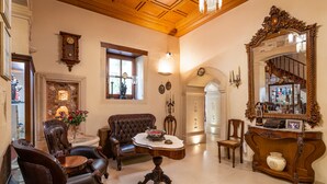 Een klassieke kamer met leren fauteuils, een houten salontafel, een grote, decoratieve spiegel en een open haard met een bloevas.