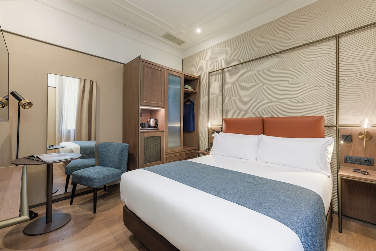 Quarto de hotel com uma cama grande, uma escrivaninha com cadeira, um guarda-roupa e um espelho.