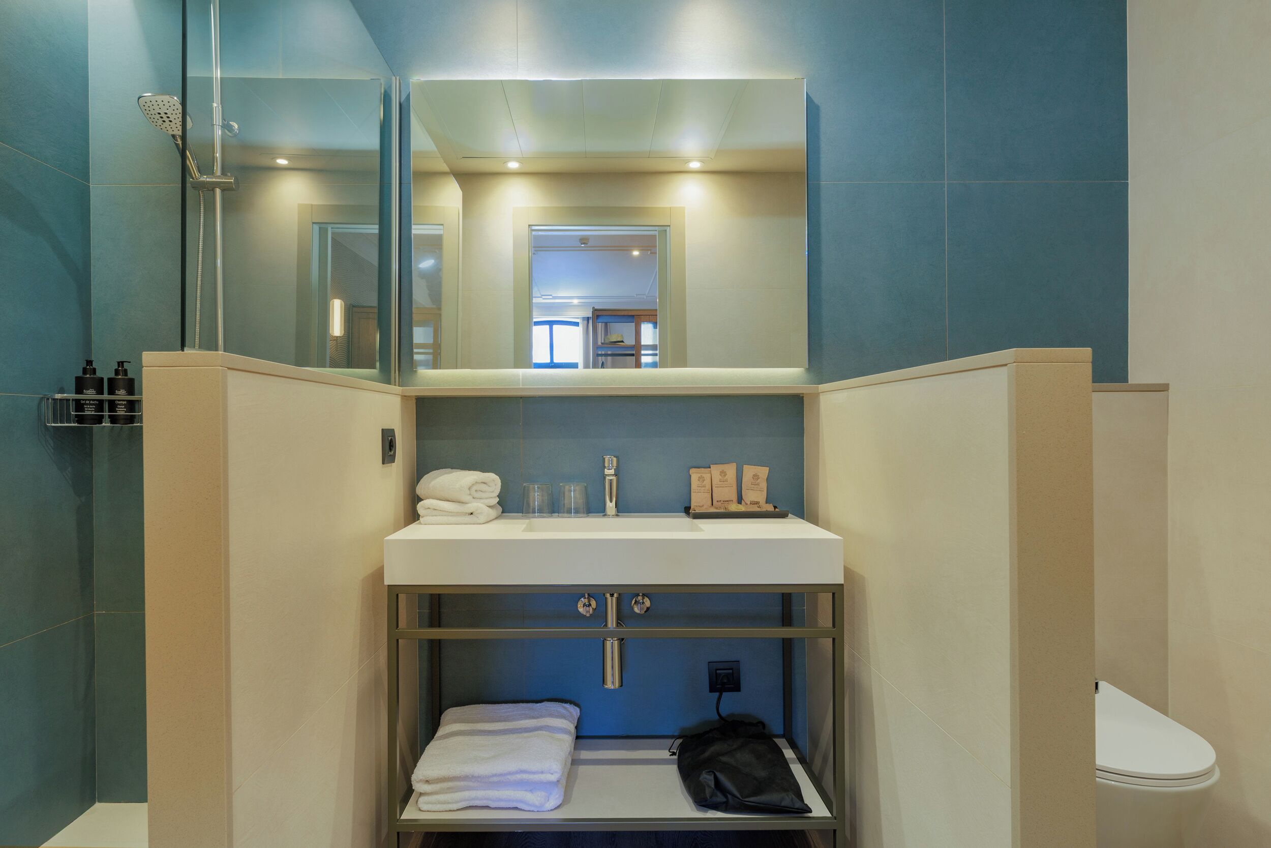 Un baño moderno con ducha envuelta en vidrio, un lavamanos blanco con espejo y un perchero para toallas.