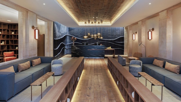 A modern lounge area with a long wooden bench, cushioned seating, and a central table. - Hotel Medinaceli (Barcelona)