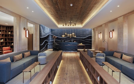 A modern lounge area with a long wooden bench, cushioned seating, and a central table.