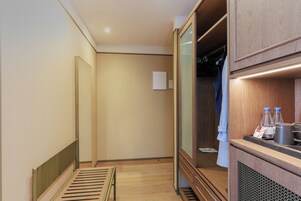 A hotel room with a wooden floor, a bed with a headboard, a wardrobe, and a small table with water bottles and a coffee mug.