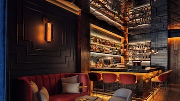 Zona de bar con un sofá rojo, un reposapiés estampado y taburetes de bar.