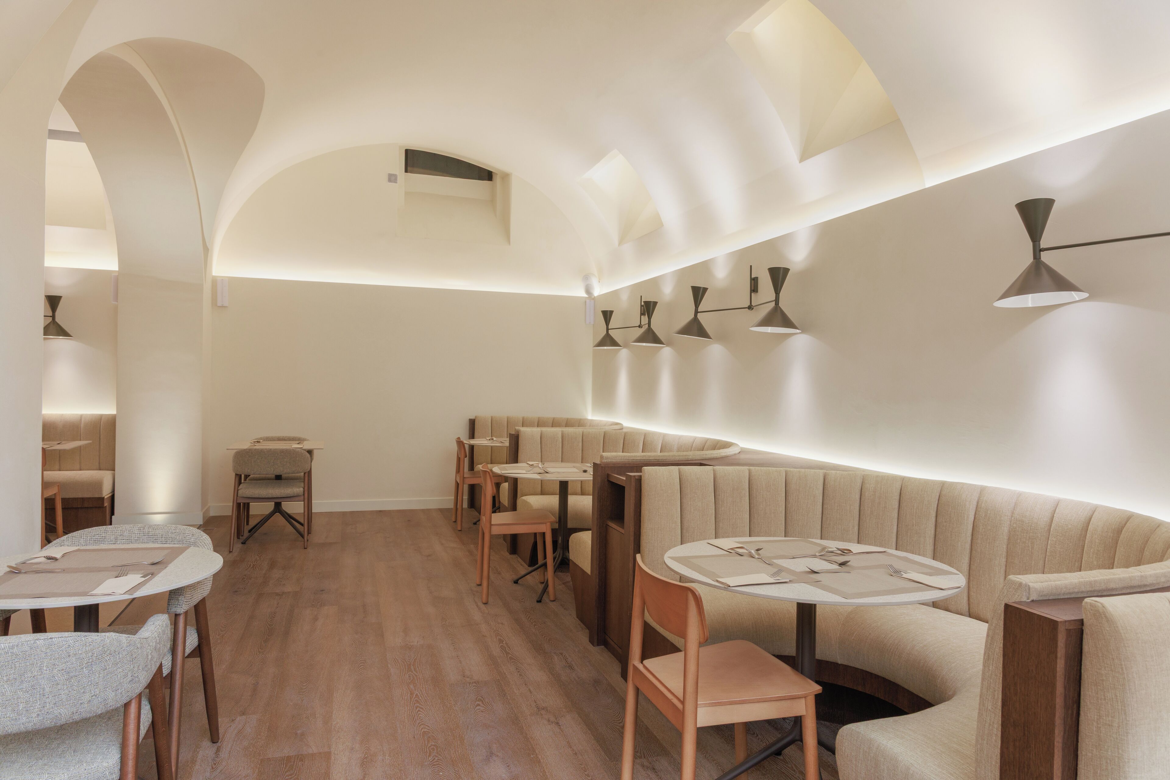 Un interior moderno con mesas redondas y asientos acolchados, pisos de madera e iluminación colgante.