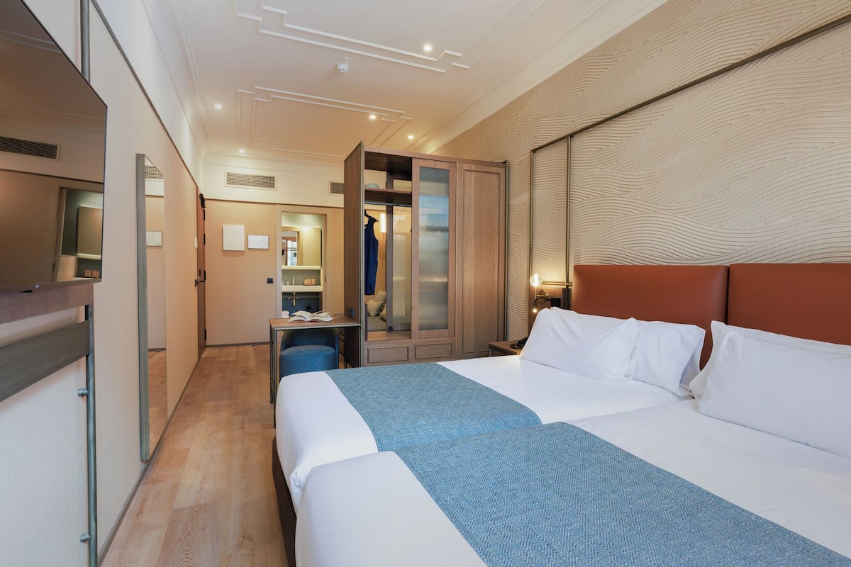 Quarto de hotel moderno com uma cama grande, um guarda-roupa, uma escrivaninha e um espelho.