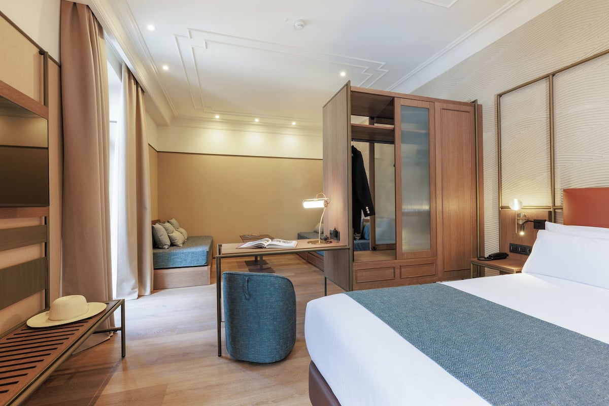 Quarto de hotel com cama, escrivaninha, cadeira, guarda-roupa e área de estar.