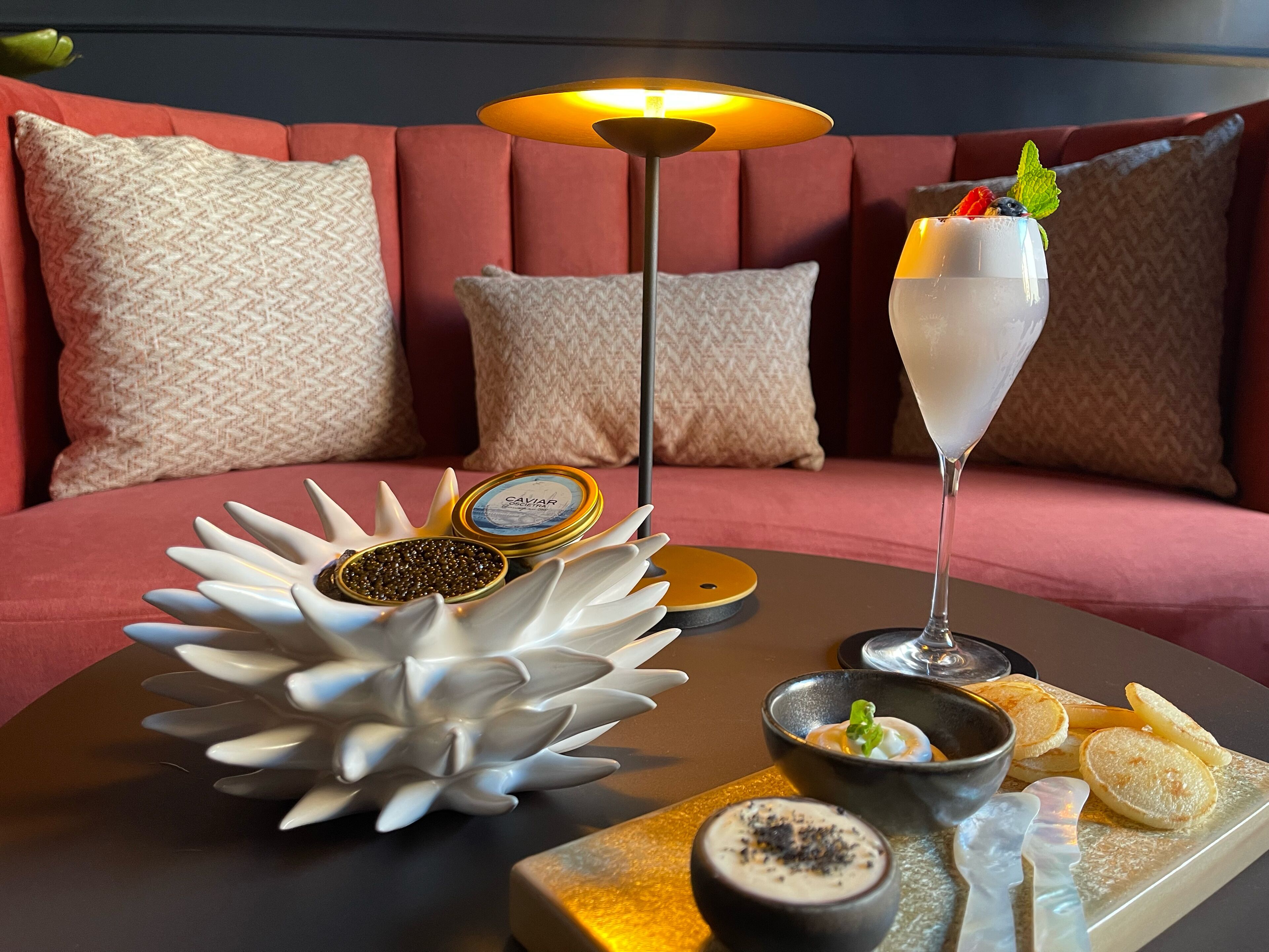 A dining table with a variety of food items, including caviar, a dessert drink, pancakes, and a bowl of soup.