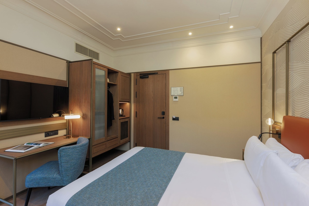 Une chambre d’hôtel comprenant un lit, un bureau avec une chaise, une armoire et un téléviseur.