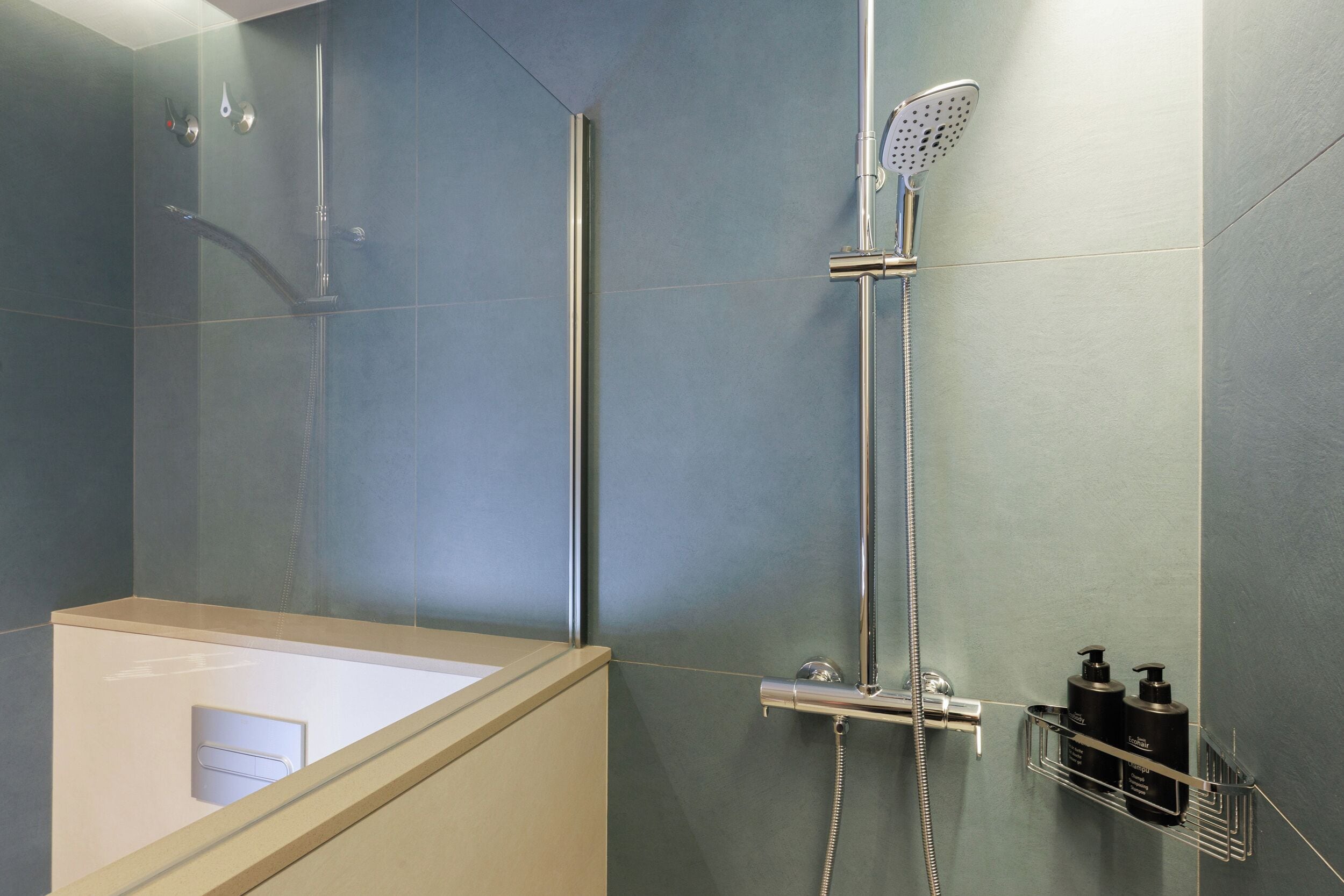 Un baño moderno con ducha de vidrio, bañera y repisa con artículos de aseo.