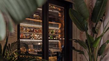 A bar area with shelves of bottles and glasses, a door leading to the bar, and potted plants.