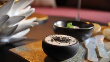 Presentación de postre con un mousse de chocolate en un bol negro, decorado con virutas de chocolate, sobre un plato de servicio texturizado.