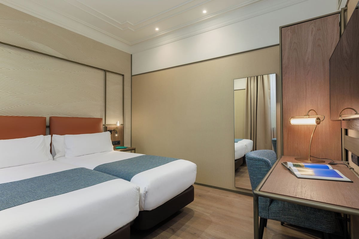Quarto de hotel com cama grande, uma escrivaninha, uma cadeira e um espelho.
