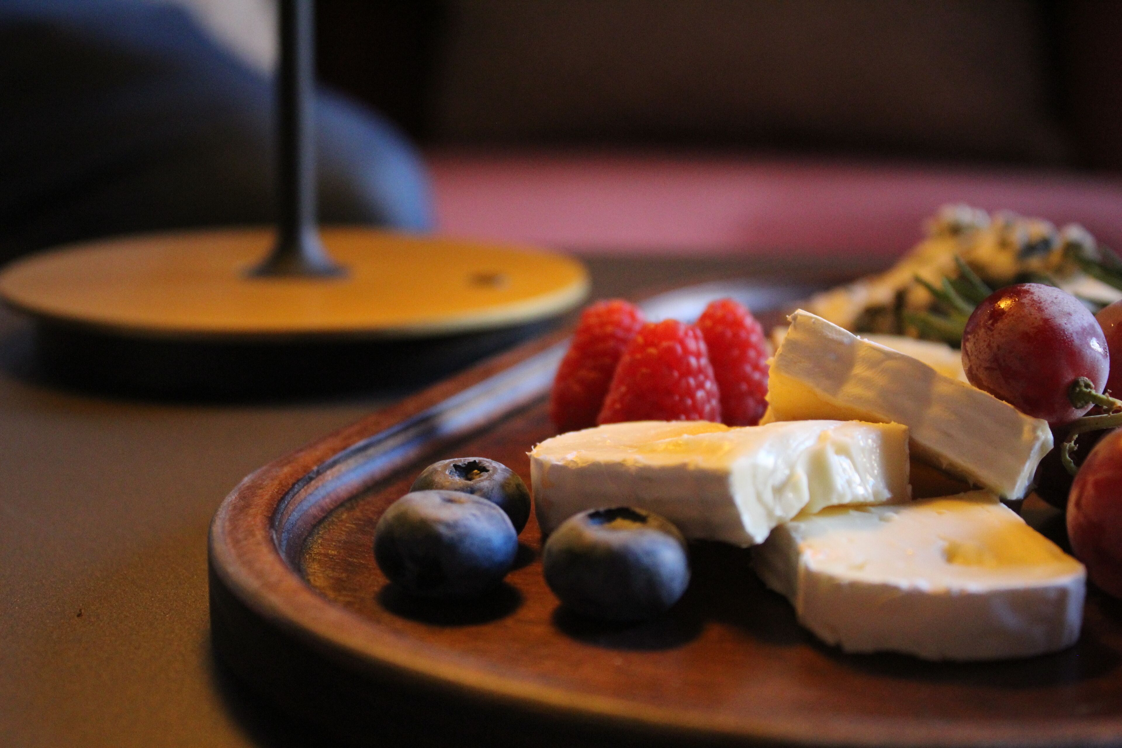 Una tabla de madera con queso, fresas y arándanos.