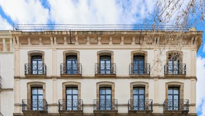 A multi-story building with a classical architectural style, featuring a symmetrical facade with evenly spaced windows and decorative iron railings on the balconies. - Hotel Medinaceli (Barcelona)