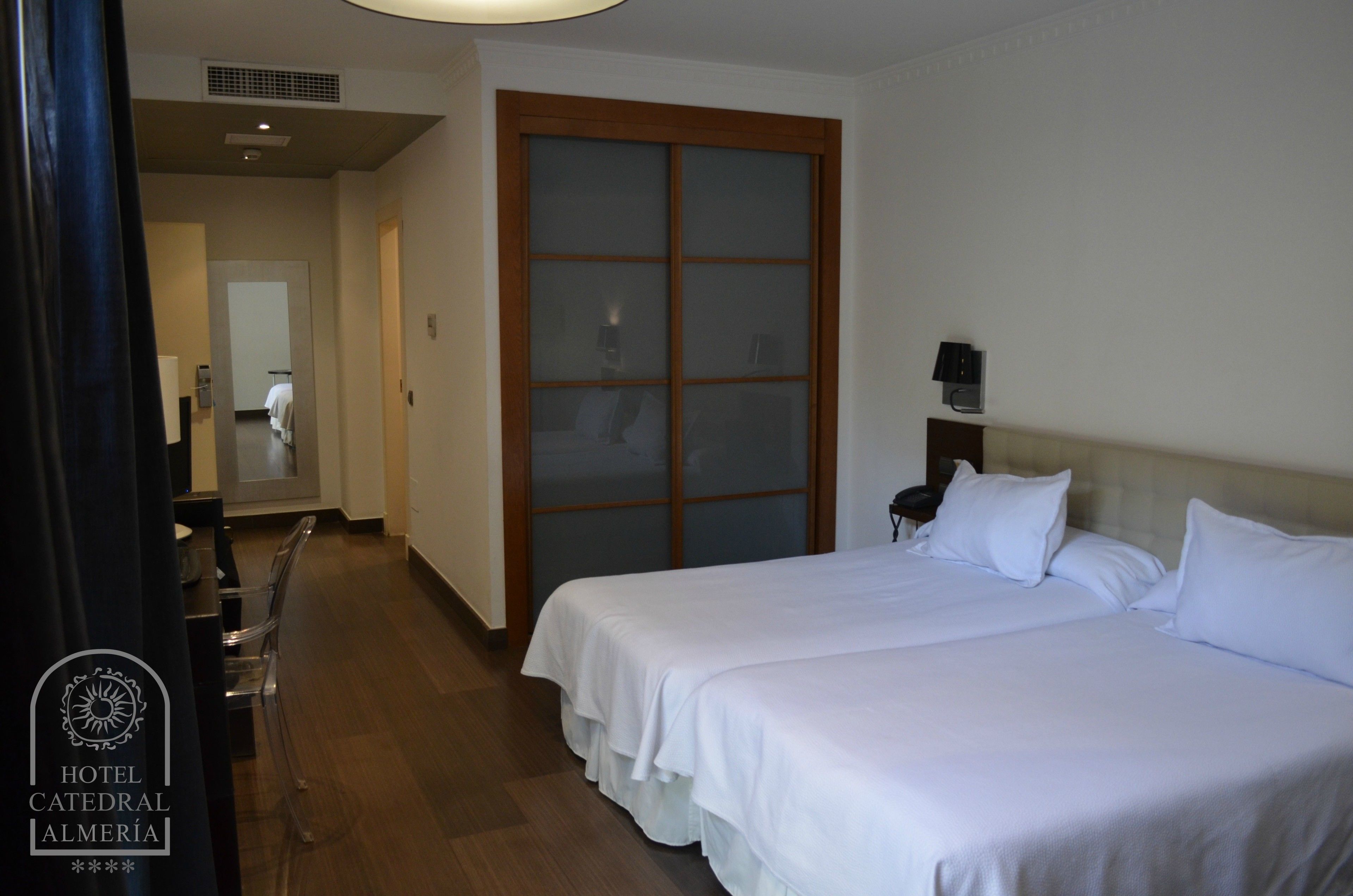 A hotel room with two beds, a wooden door, a desk with a chair, and a mirror.