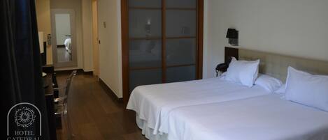 A hotel room with two beds, a wooden door, a desk with a chair, and a mirror.