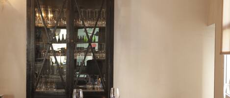 A dining area with a table set for two, a cabinet with glassware, and chairs.