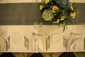 Una mesa dispuesta para una comida con platos, cubiertos y vasos, y un centro de mesa floral.