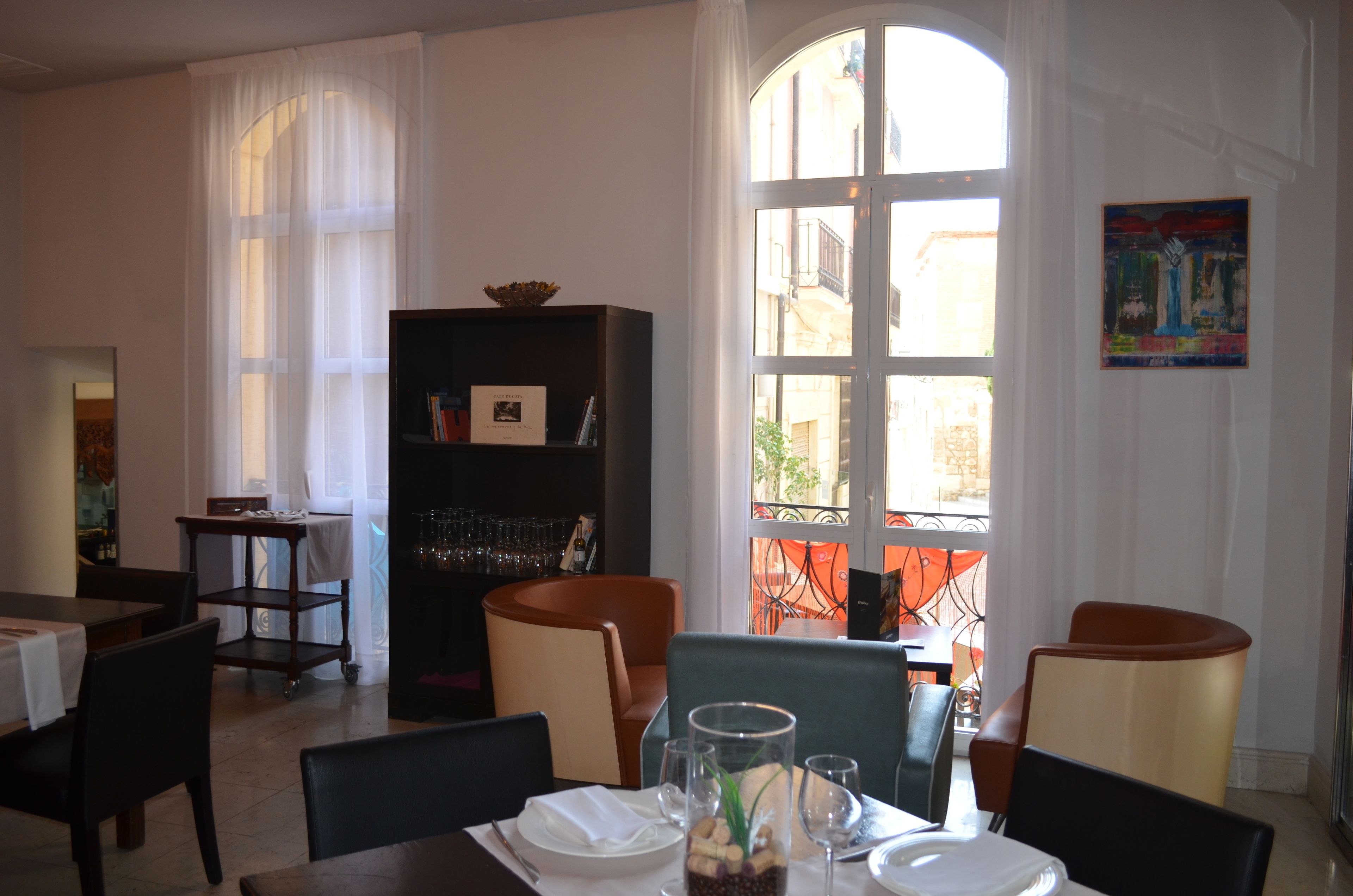 A dining area with a table set for two, a bookshelf, and a view of the outside through a large window.