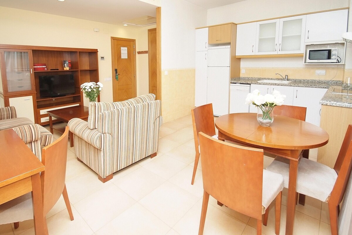 A living room with a TV, sofa, and dining area with chairs and a table.