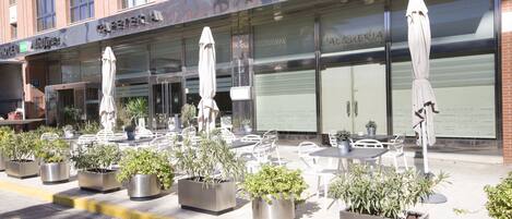 A restaurant with outdoor seating, potted plants, and a brick building facade.