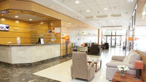 A hotel lobby with a reception desk, seating area, and a large window. - Albufera Apartotel (Alfafar)