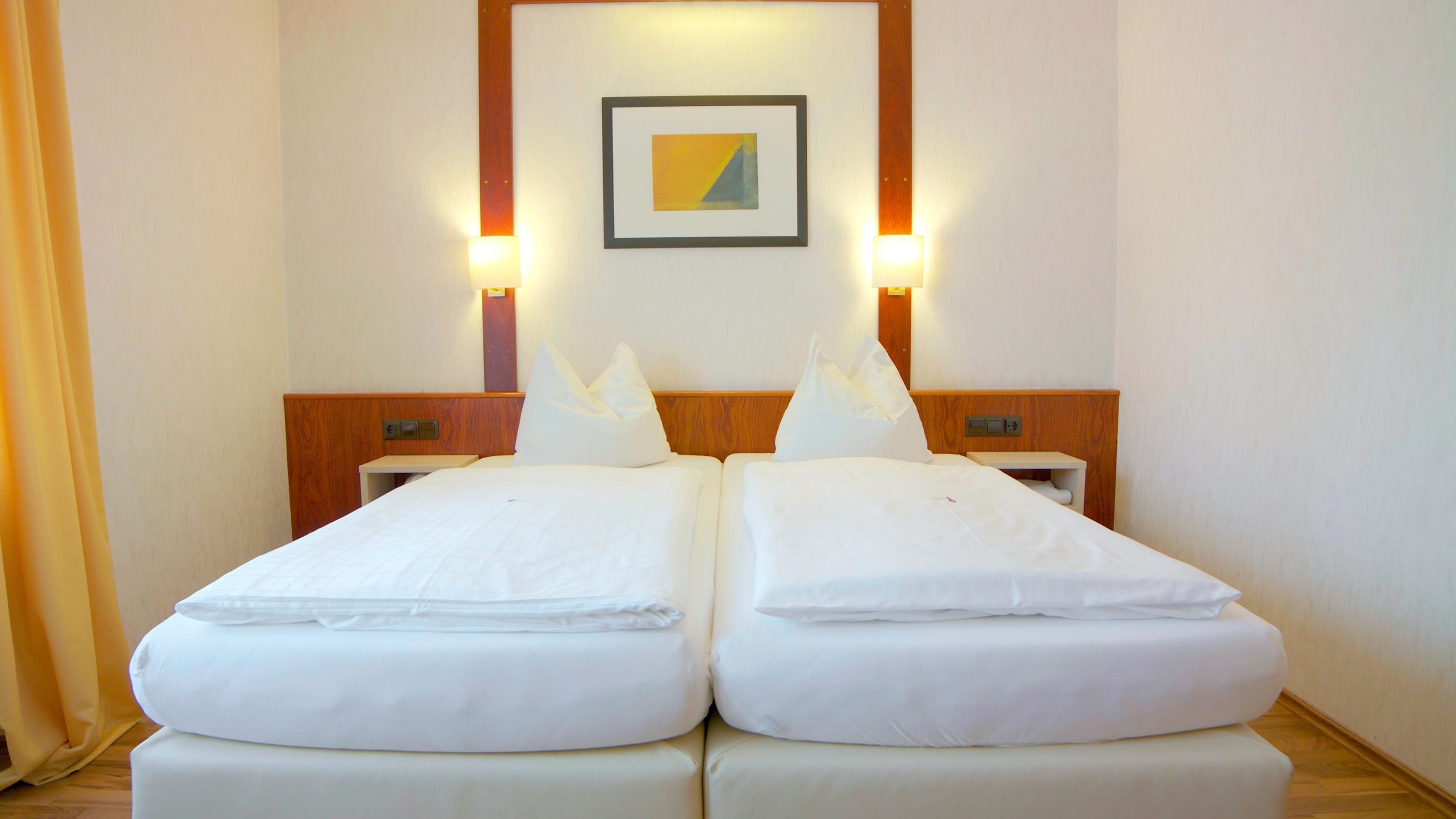 A double bed with white linens, a wooden headboard, two bedside tables, and a framed picture on the wall.