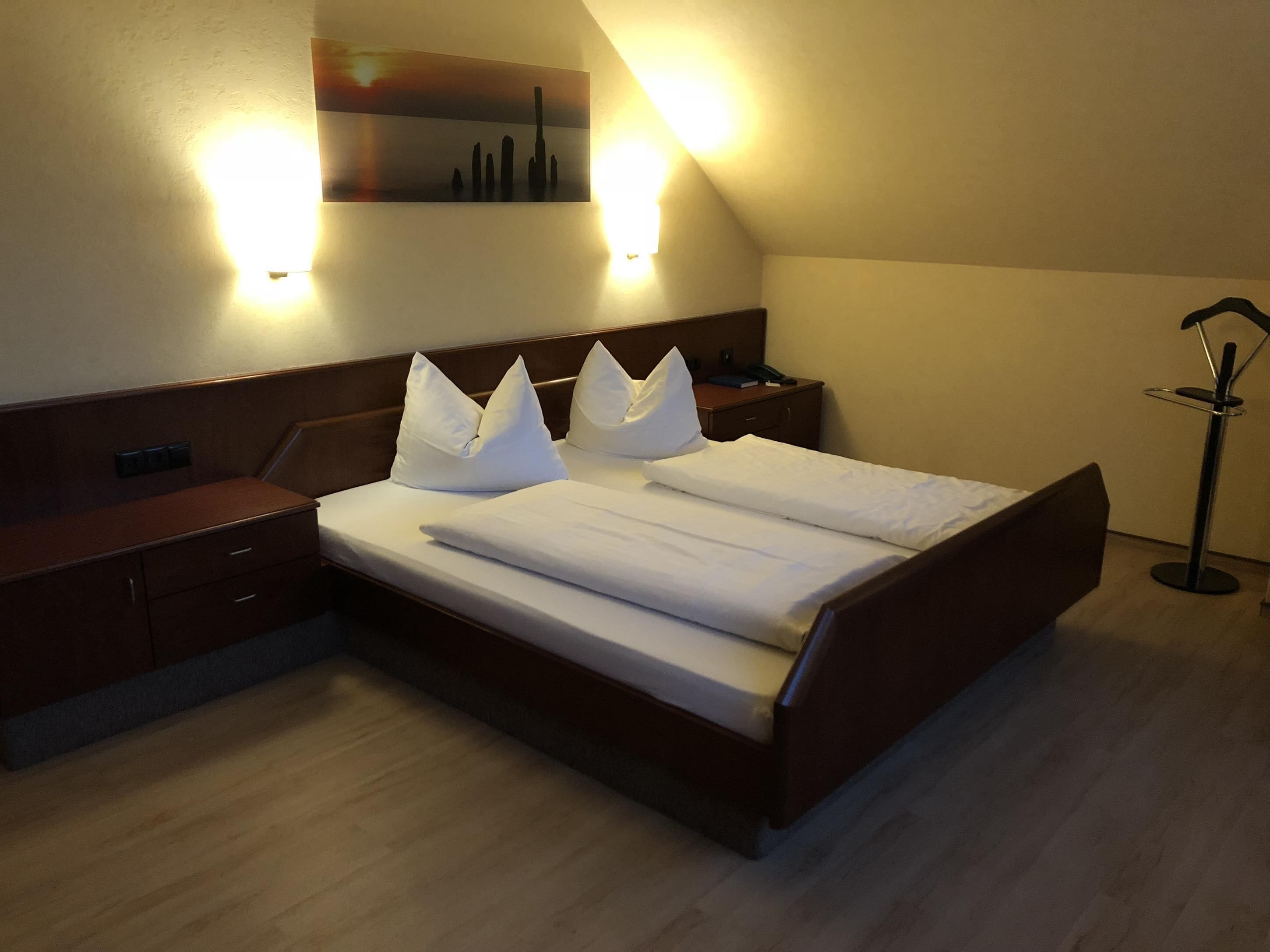 Ein Hotelzimmer mit Bett, Nachttischen, einer Lampe und einem an der Wand hängenden Kunstwerk.