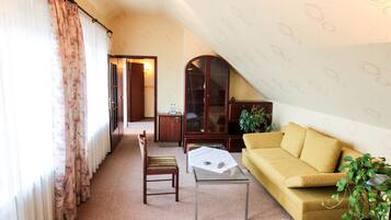 A cozy living room with a yellow sofa, a glass coffee table, a wooden chair, and a large arched cabinet.