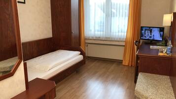 Ein Hotelzimmer mit einem hölzernen Bett, einem Schreibtisch mit Computer, einem Fenster mit Vorhängen und einer Heizung.
