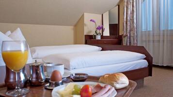 Habitación de hotel con cama bien hecha, bandeja de desayuno con huevos, tostadas y fruta, y una ventana con cortinas.