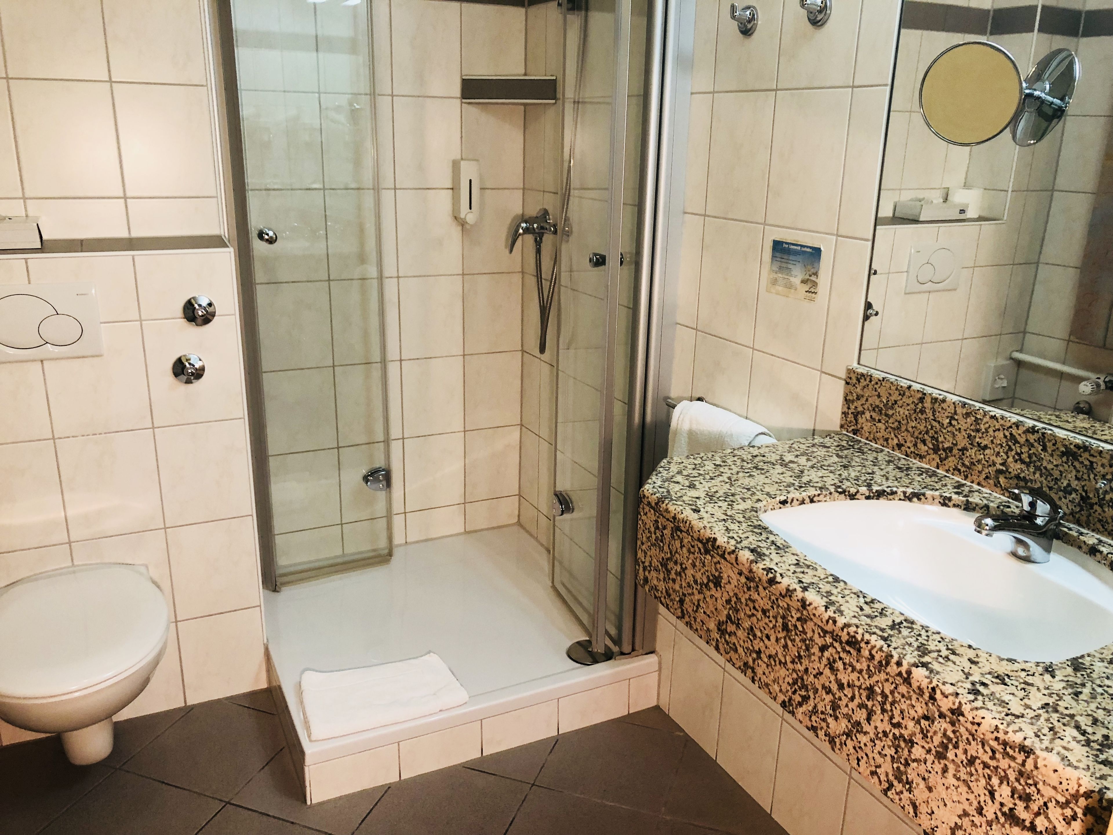 A bathroom with a shower, toilet, sink, and a mirror.